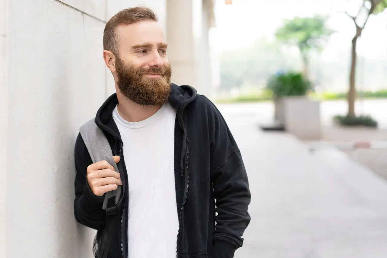 Młody mężczyzna w białym T-shircie, czarnej rozpinanej bluzie z kapturem i plecakiem